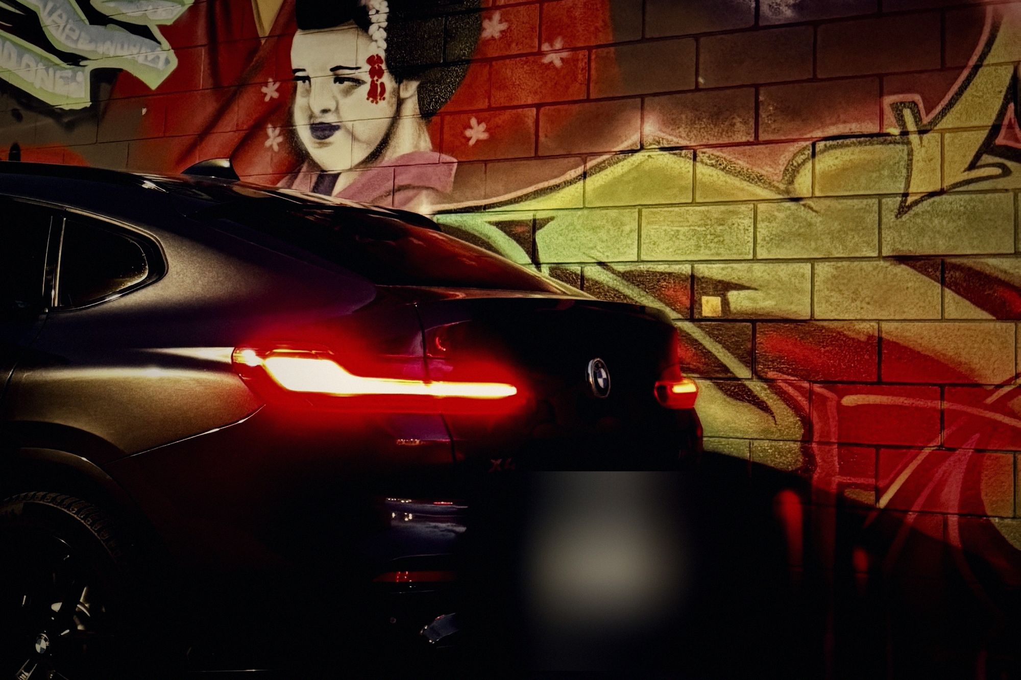 The same X4 at night, tail lights glowing in front of a graffiti mural